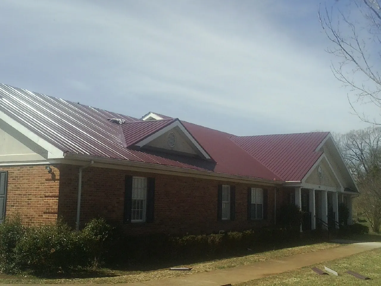 Red metal roof with gabled entries on a long brick building, from a Hail Damage Roof Repair job in Hestand