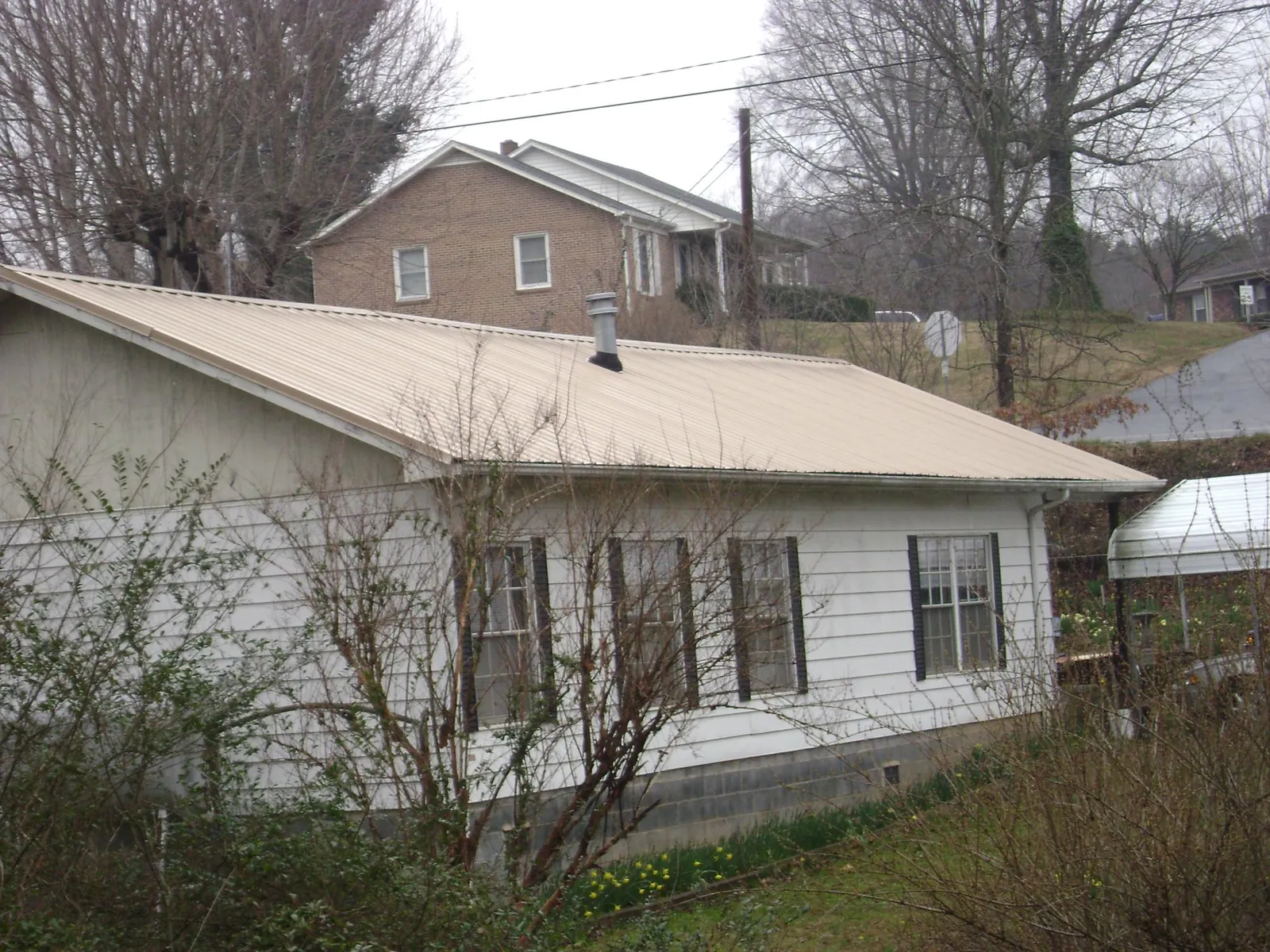 Tan metal roof on a white sided house set into a hillside — Commercial Roofing by Roofing Brothers in Hestand